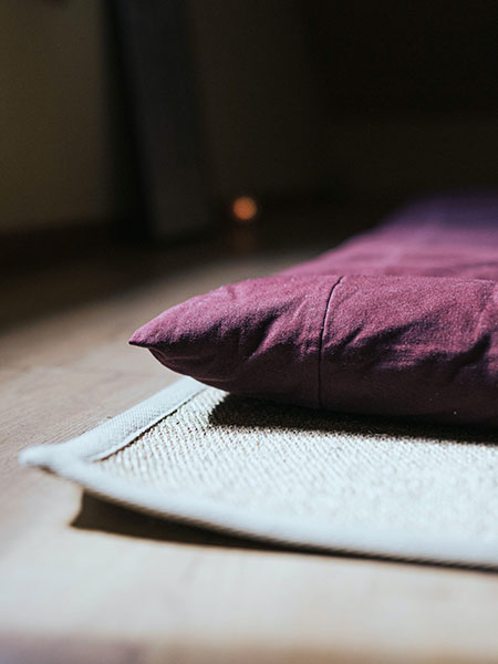 Bord d'un futon de couleur violette posé sur un tapis tissé gris